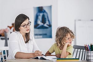 Mutter mit genervtem Kind bei Hausaufgaben am Tisch